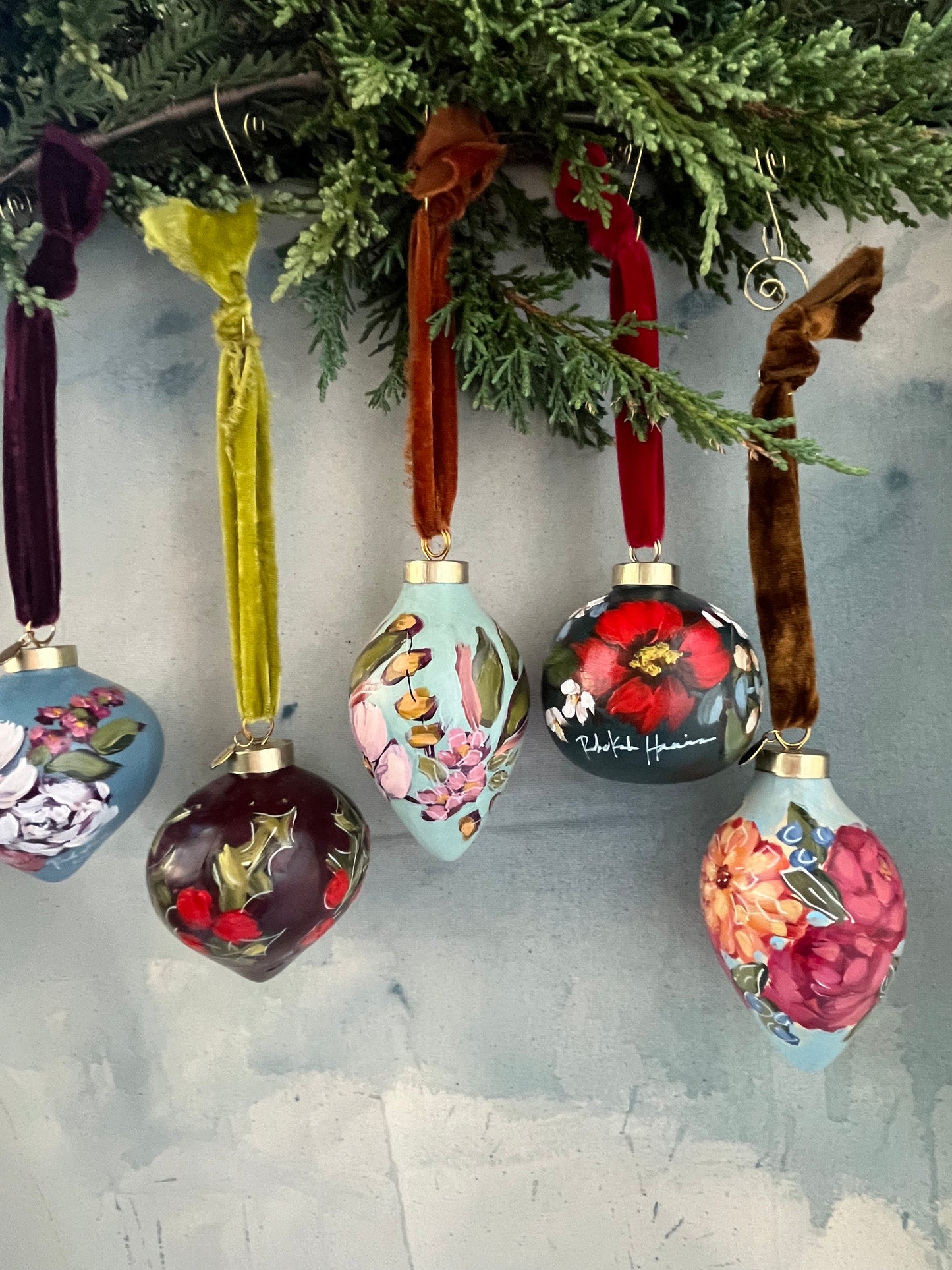 Decorative Christmas ornaments with floral designs hanging on a tree branch.