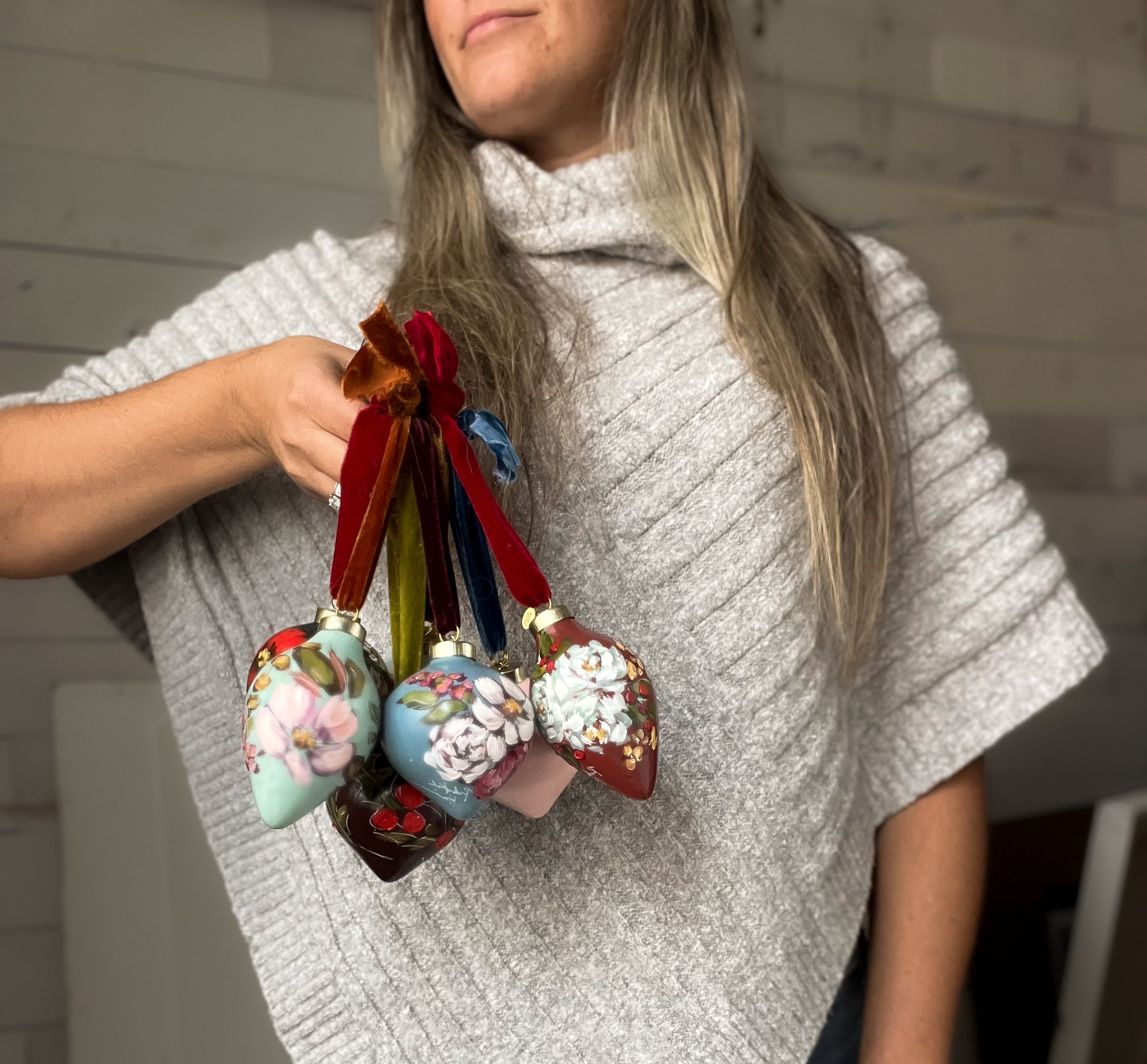 Person holding decorative Christmas ornaments with ribbons against a neutral background